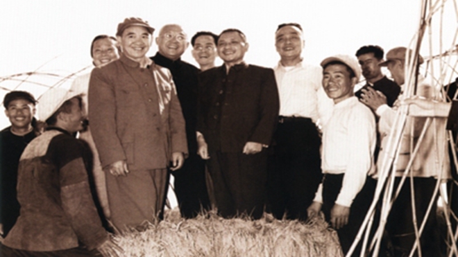 1958年10月18日,邓小平由人托扶,站在稻子上与人合影留念。(资料图片)